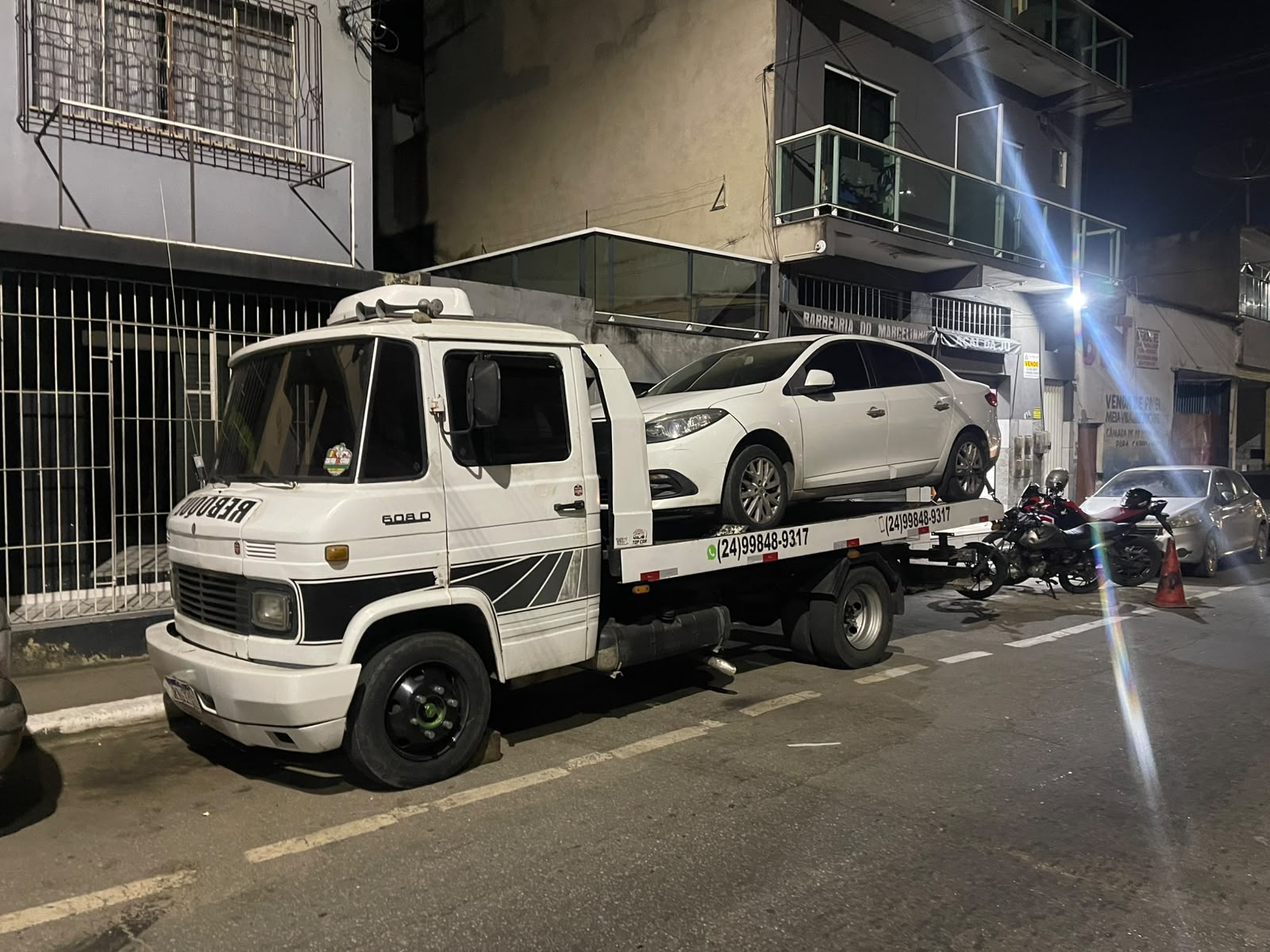 Guincho plataforma Mercedes 608D carregando carro à noite com telefone visível