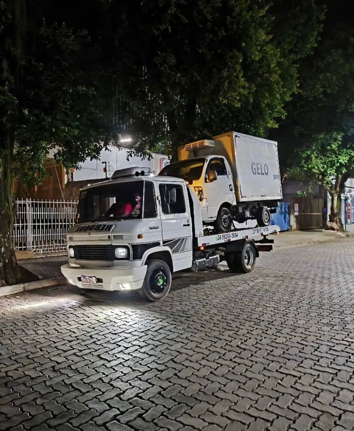 Guincho rebocando caminhão refrigerado à noite